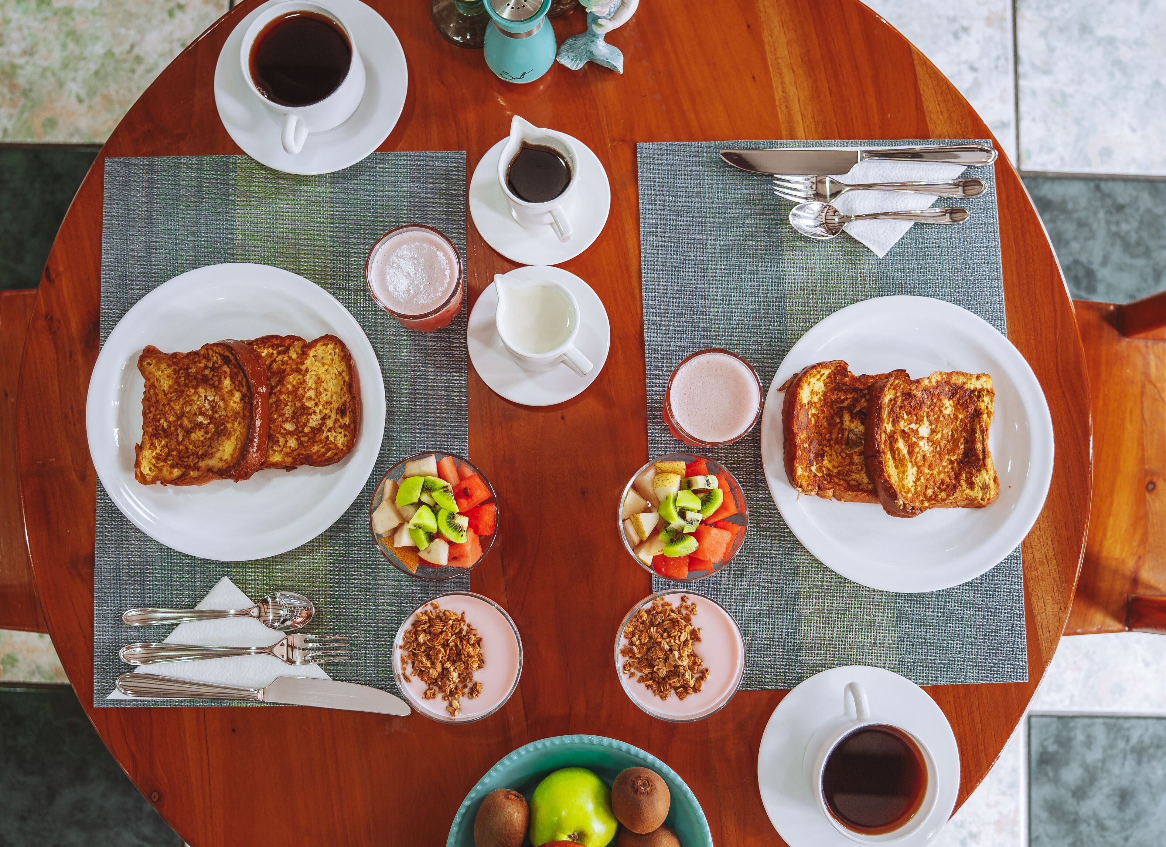 Desayuno con tostadas, fruta, yogur y café sobre una mesa de madera.