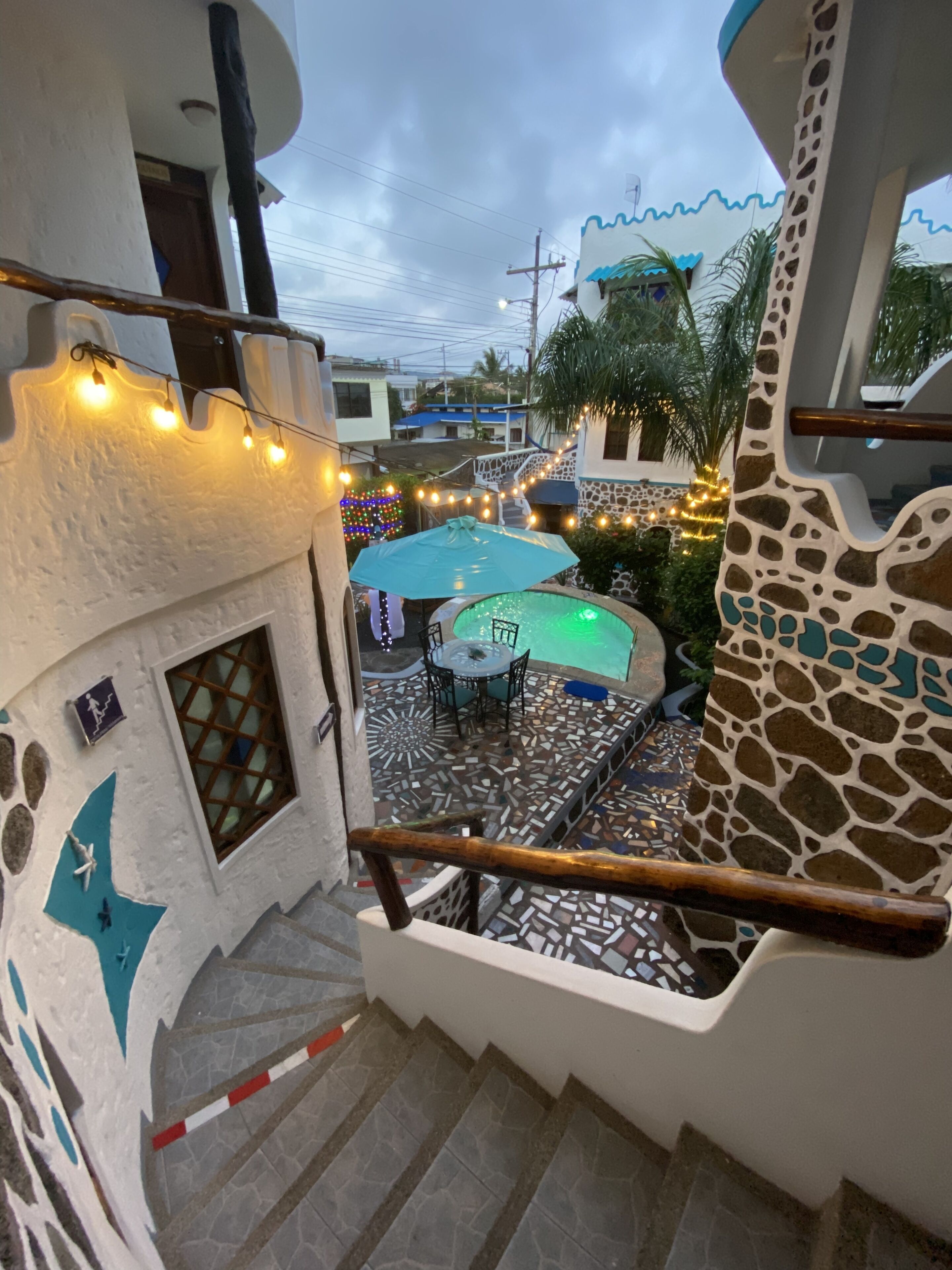 Una escalera conduce a un área de piscina con piso de baldosas, rodeada por un muro blanco con detalles decorativos y una palmera.