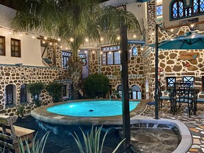 Un patio con piscina, muros de piedra, palmeras y mobiliario exterior.