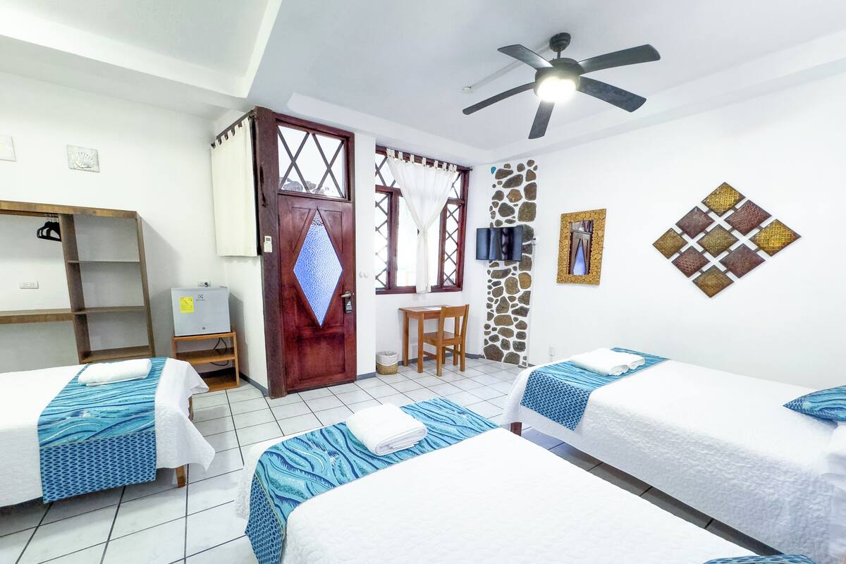 Ein Hotelzimmer mit zwei Betten, einer Holztür, einer Steinwand, einem Fernseher und einem Deckenventilator.