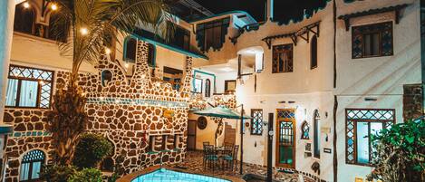 A courtyard with a swimming pool, stone walls, and a palm tree.