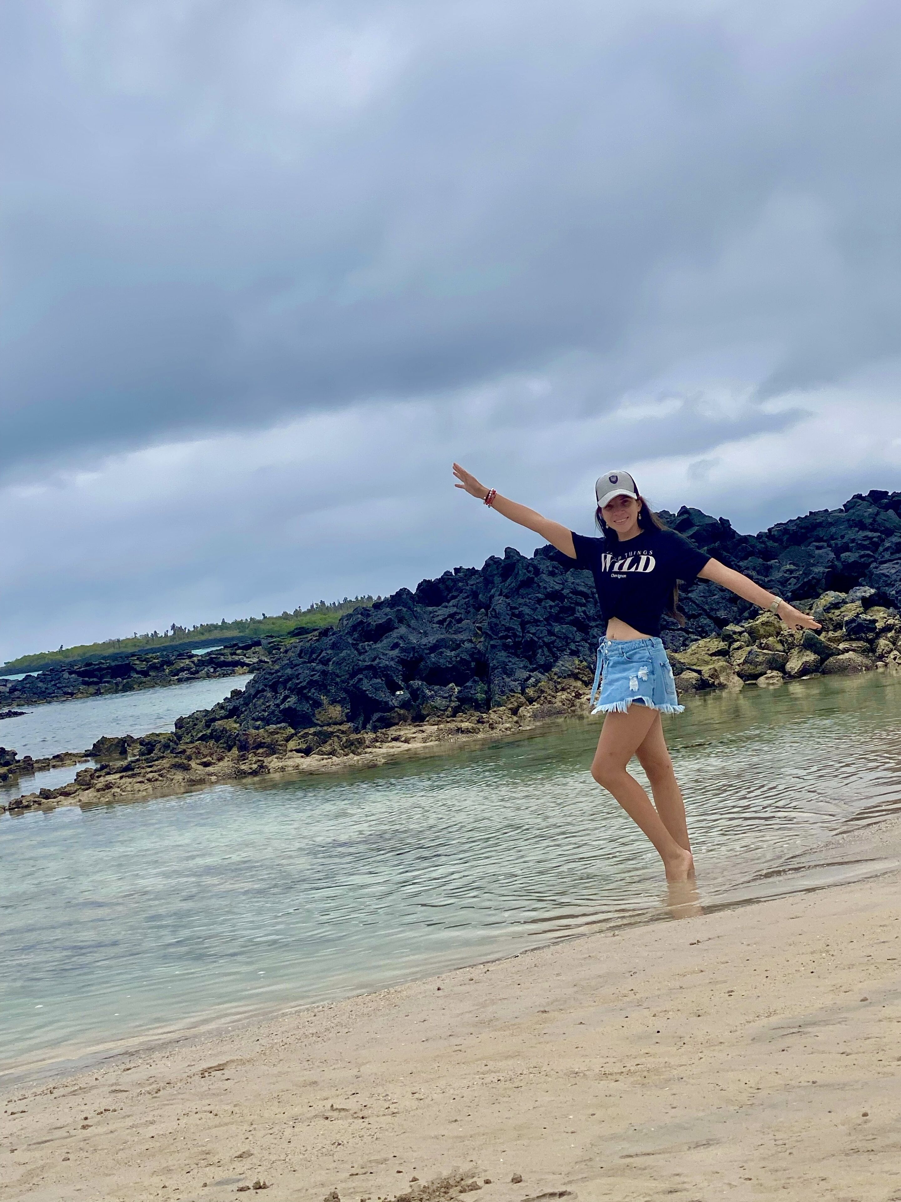 Une personne qui danse sur une plage, avec des formations rocheuses en arrière-plan.