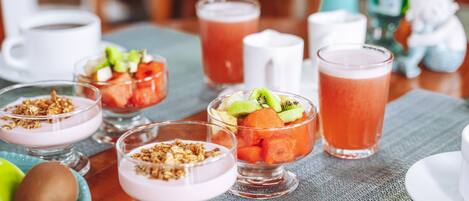 A table with various food items and drinks, including bowls of yogurt with granola, a fruit salad, and a glass of juice.