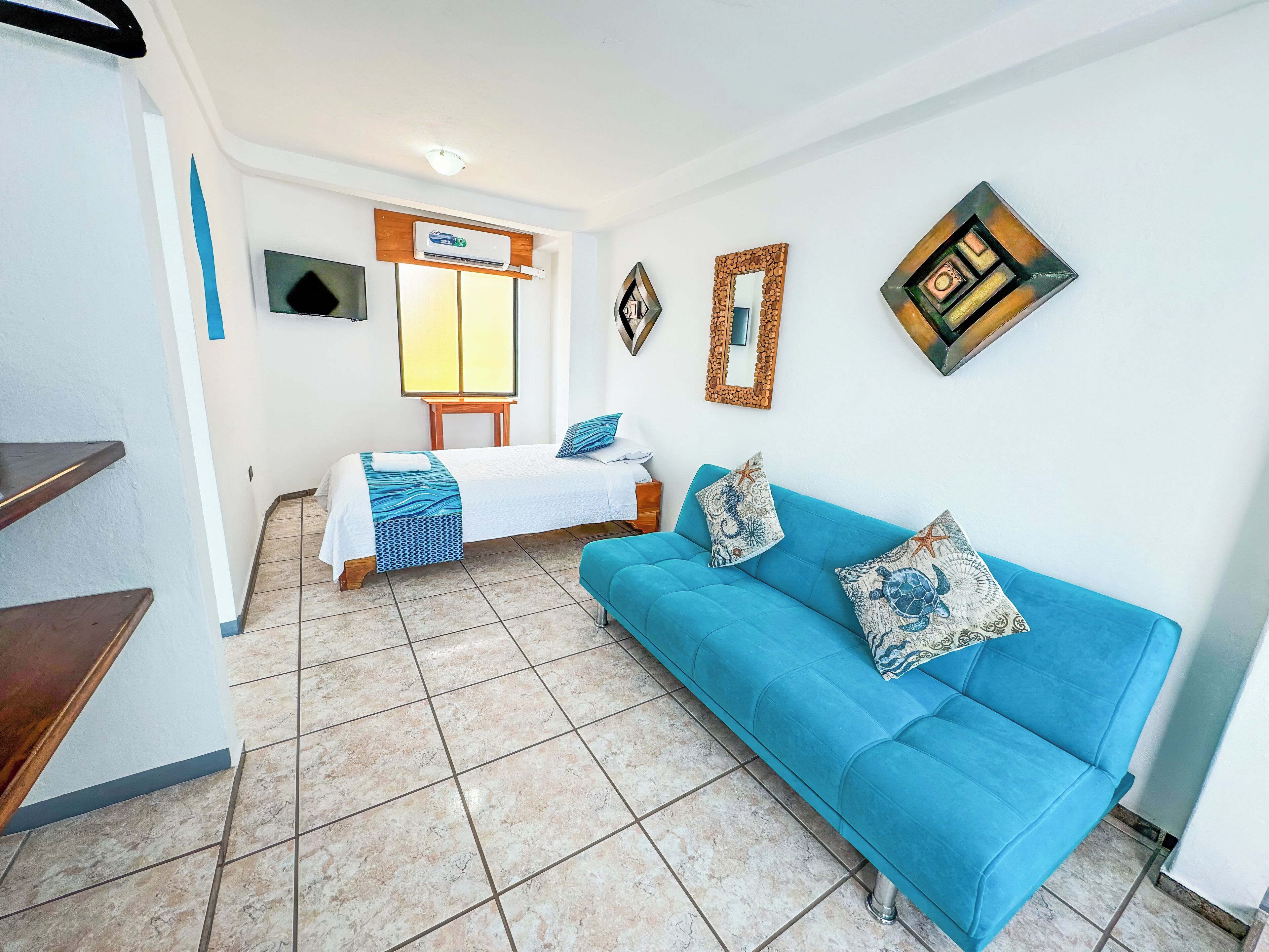 Une chambre d’hôtel avec un lit, un canapé bleu, une télévision et une fenêtre donnant sur un beau paysage.