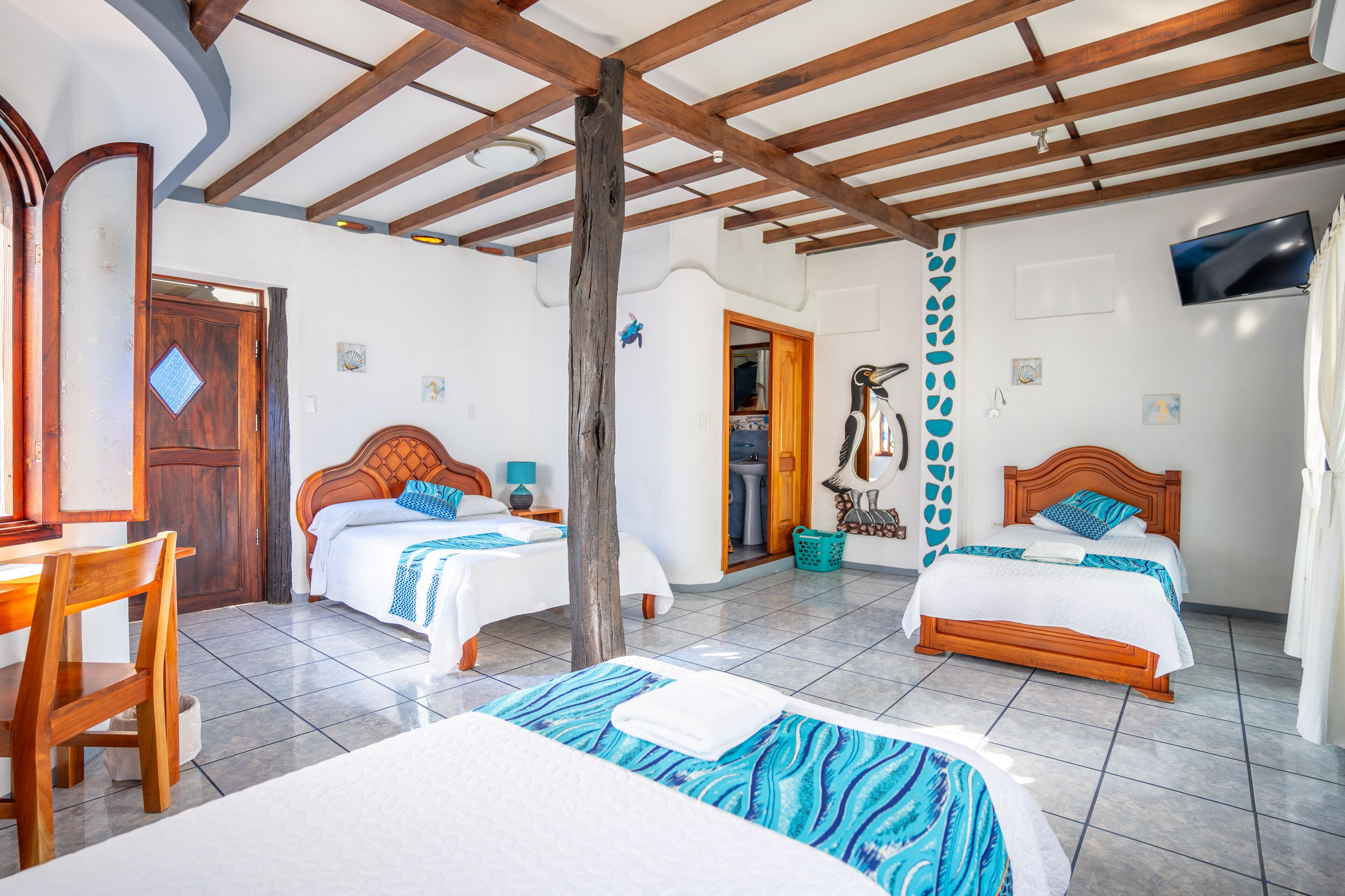 A hotel room with two beds, a wooden ceiling, a TV, and a bathroom visible through an open door.