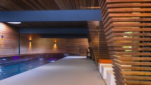 Un área de piscina interior moderna con una pared de listones de madera a la derecha y suelo de baldosas.