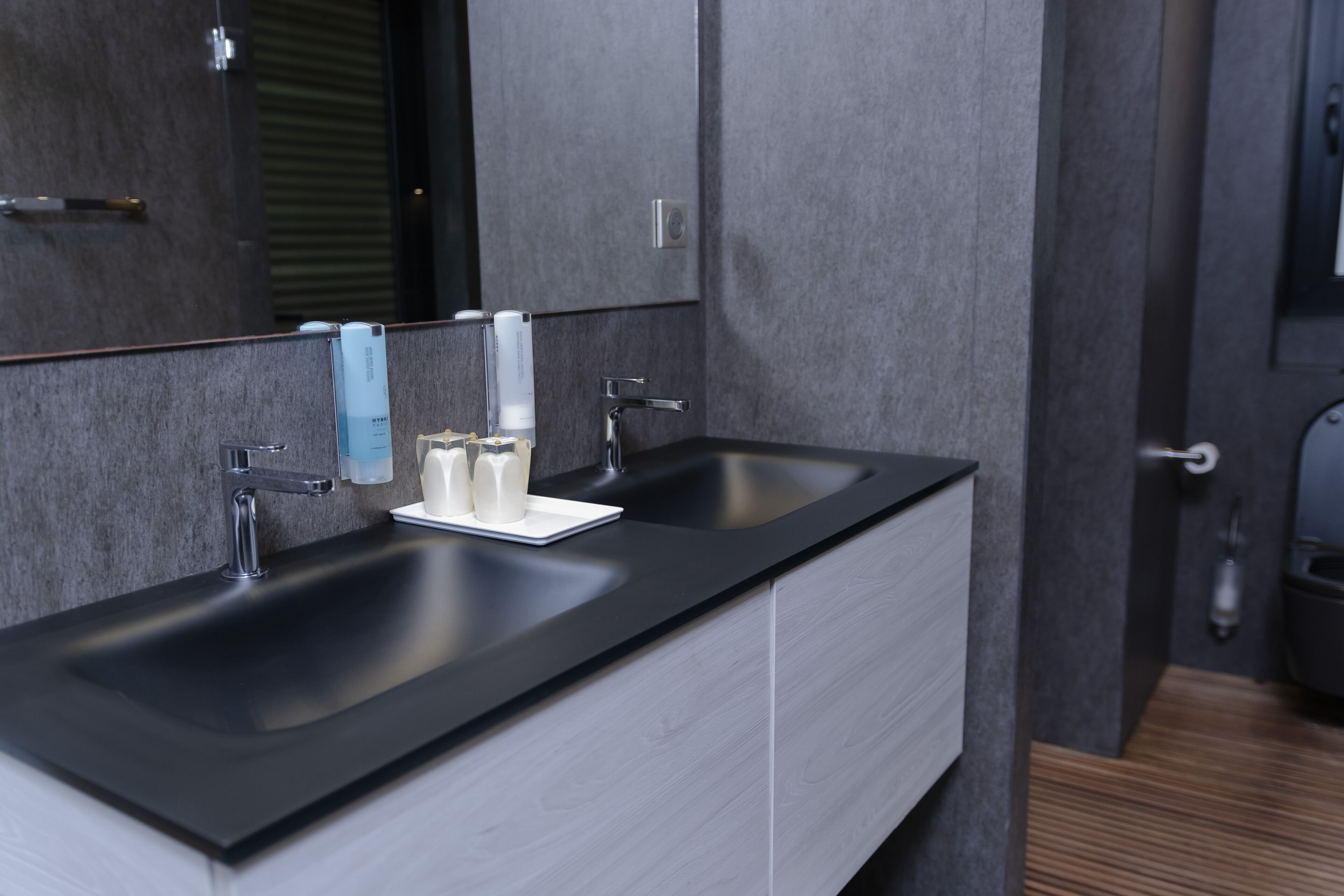 A modern bathroom with a black sink, a mirror, and a towel dispenser.