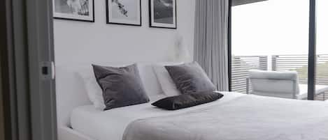 Un dormitorio moderno con una cama grande, ropa de cama blanca y vistas al exterior a través de un amplio ventanal.