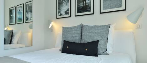 A neatly arranged bedroom with a large bed, two pillows, a bedside lamp, and three framed pictures on the wall.