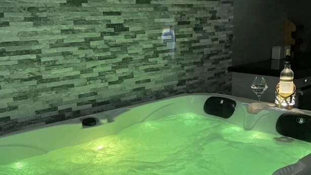 A hot tub with a control panel, a glass bottle, and a wine glass on a counter.