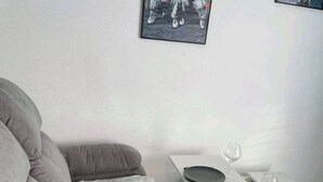 A modern living room with a grey sofa, a white coffee table, and a dining table with chairs.