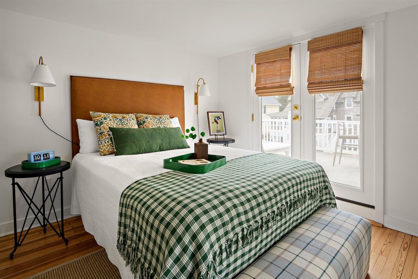 Quarto de hotel com uma cama grande, uma mesa de cabeceira com luminária, um relógio e uma janela com persianas.