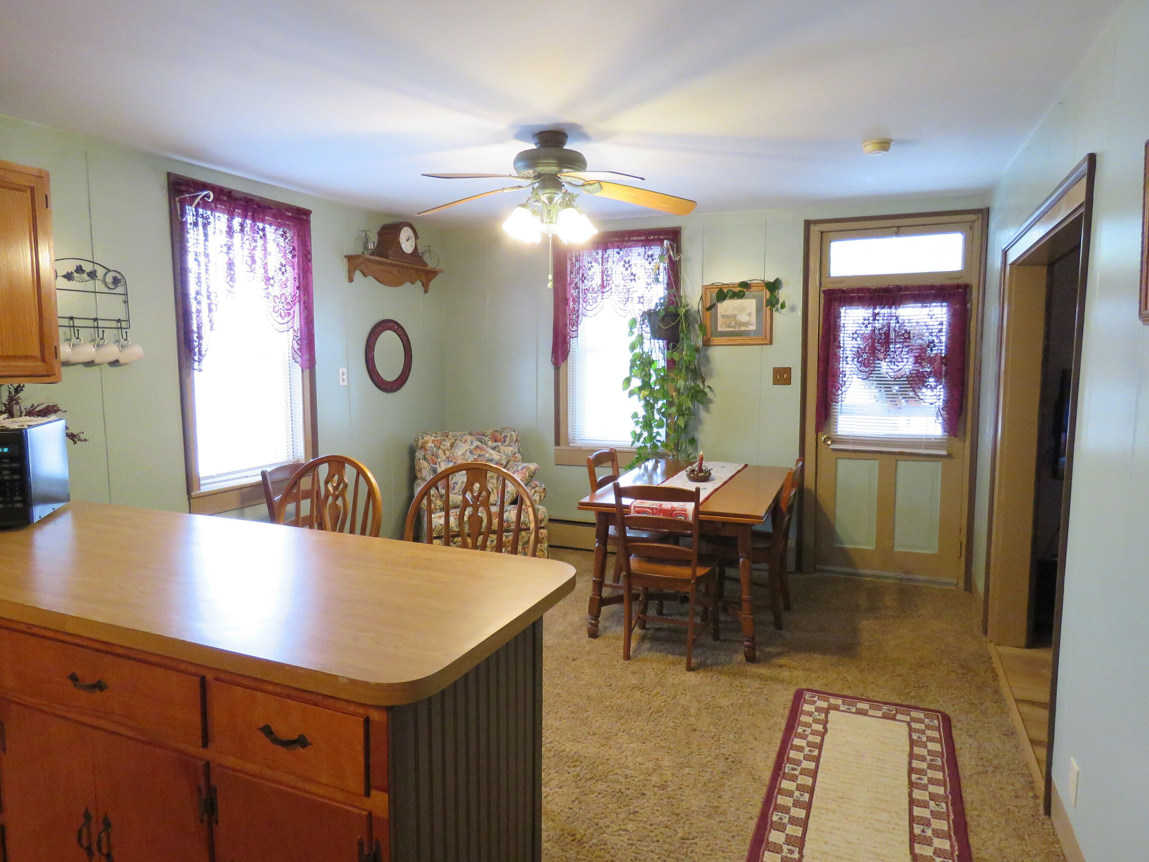 A kitchen with a wooden counter, dining table, chairs, and a ceiling fan.