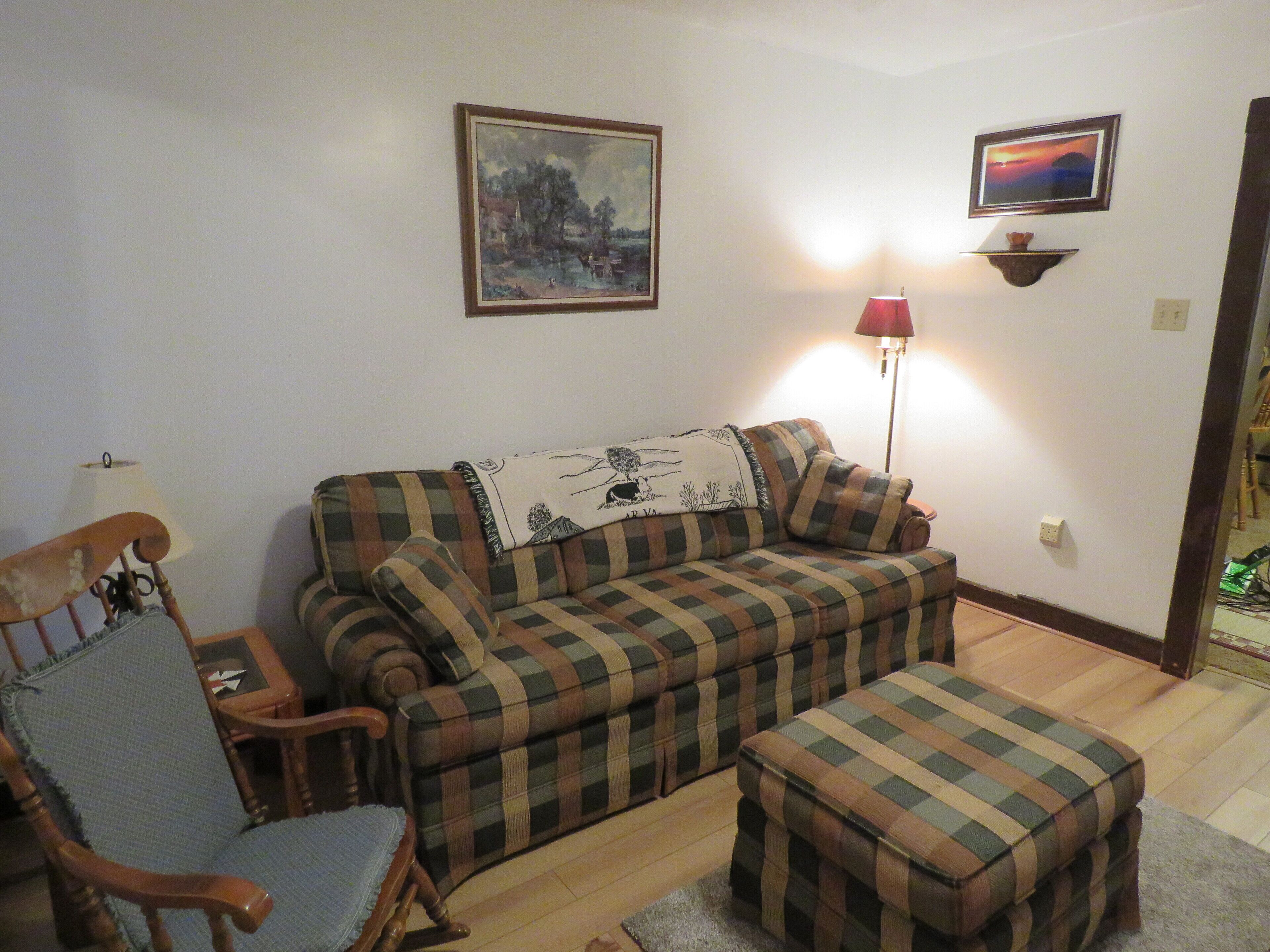 A living room with a plaid sofa, a wooden chair, a small table, and two wall-mounted lamps.