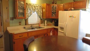 A kitchen with wooden cabinets, a double sink, a refrigerator, and a dining table with chairs.