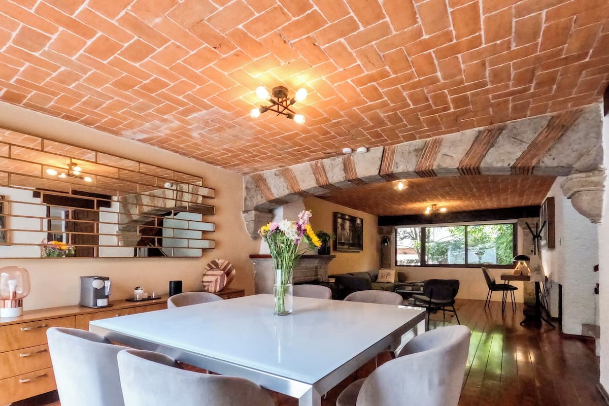 Un comedor espacioso con techo de ladrillo, una mesa blanca y cuatro sillas.