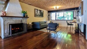 A living room with a fireplace, a sofa, a chair, and a dining area with a table and chairs. - Mi Zona Lodging Coyoacán (Mexico City)