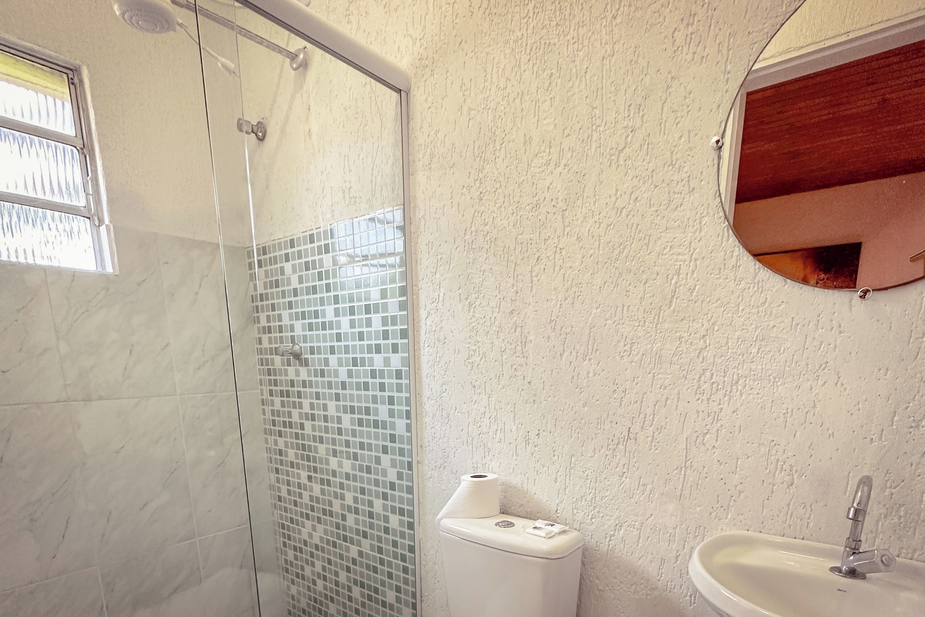Une salle de bain avec une douche à parois de verre, des toilettes dotées d’un porte-serviettes en papier et un lavabo avec un miroir au-dessus.