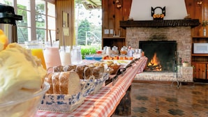 A breakfast buffet with various food items and beverages, a fireplace, and a checkered tablecloth. - Pousada Casa de Campos Capivari by Concavus (Campos do Jordão)