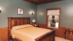 Une chambre à coucher avec un lit en bois, une table de chevet, une lampe fixée au mur, un tableau encadré et une fenêtre donnant sur l’extérieur.