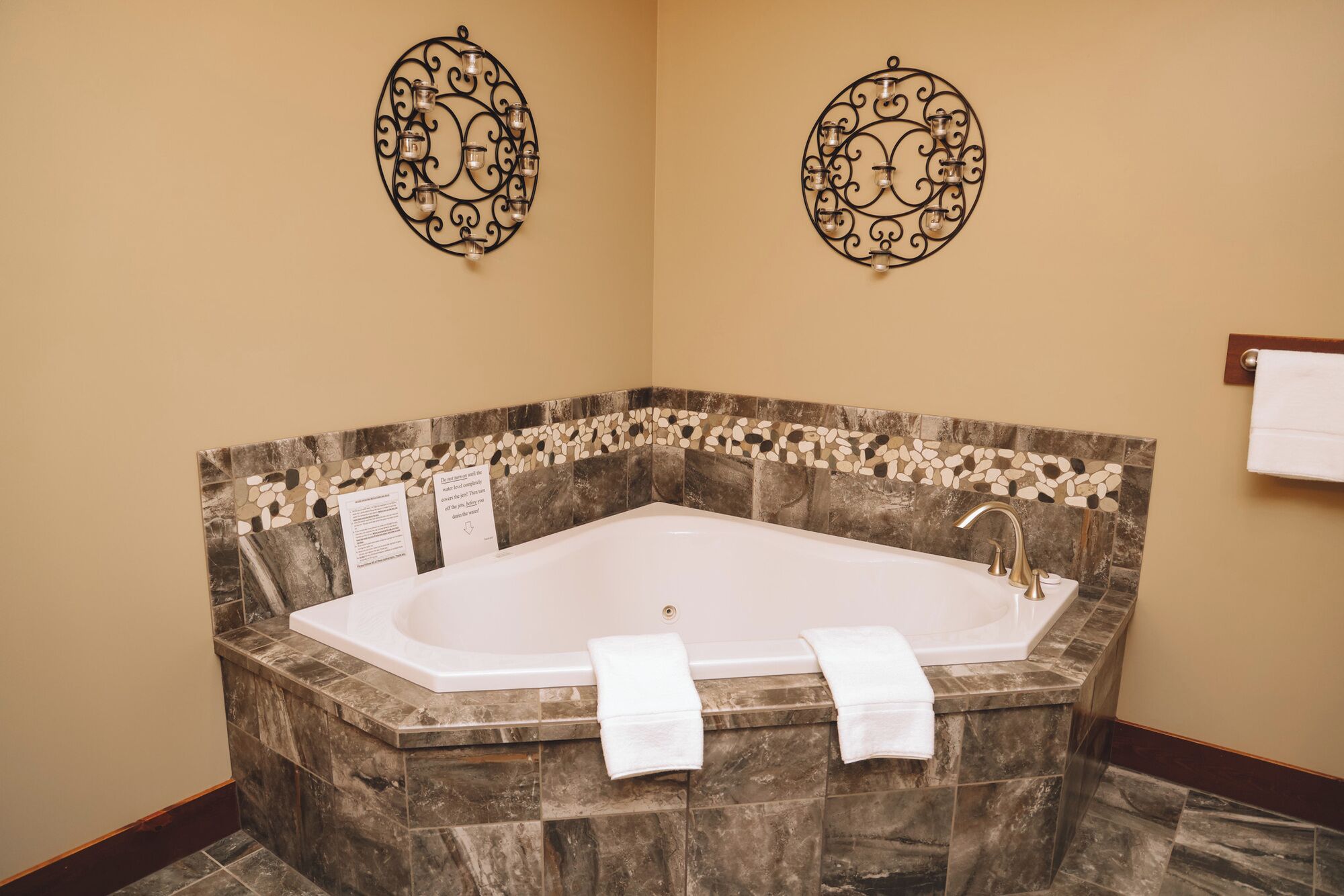 A large freestanding bathtub with a marble surround, two wall sconces, and a towel rack.