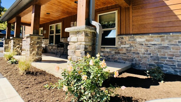 Un bâtiment en bois doté de piliers en pierre, de grandes fenêtres et d’un patio couvert.