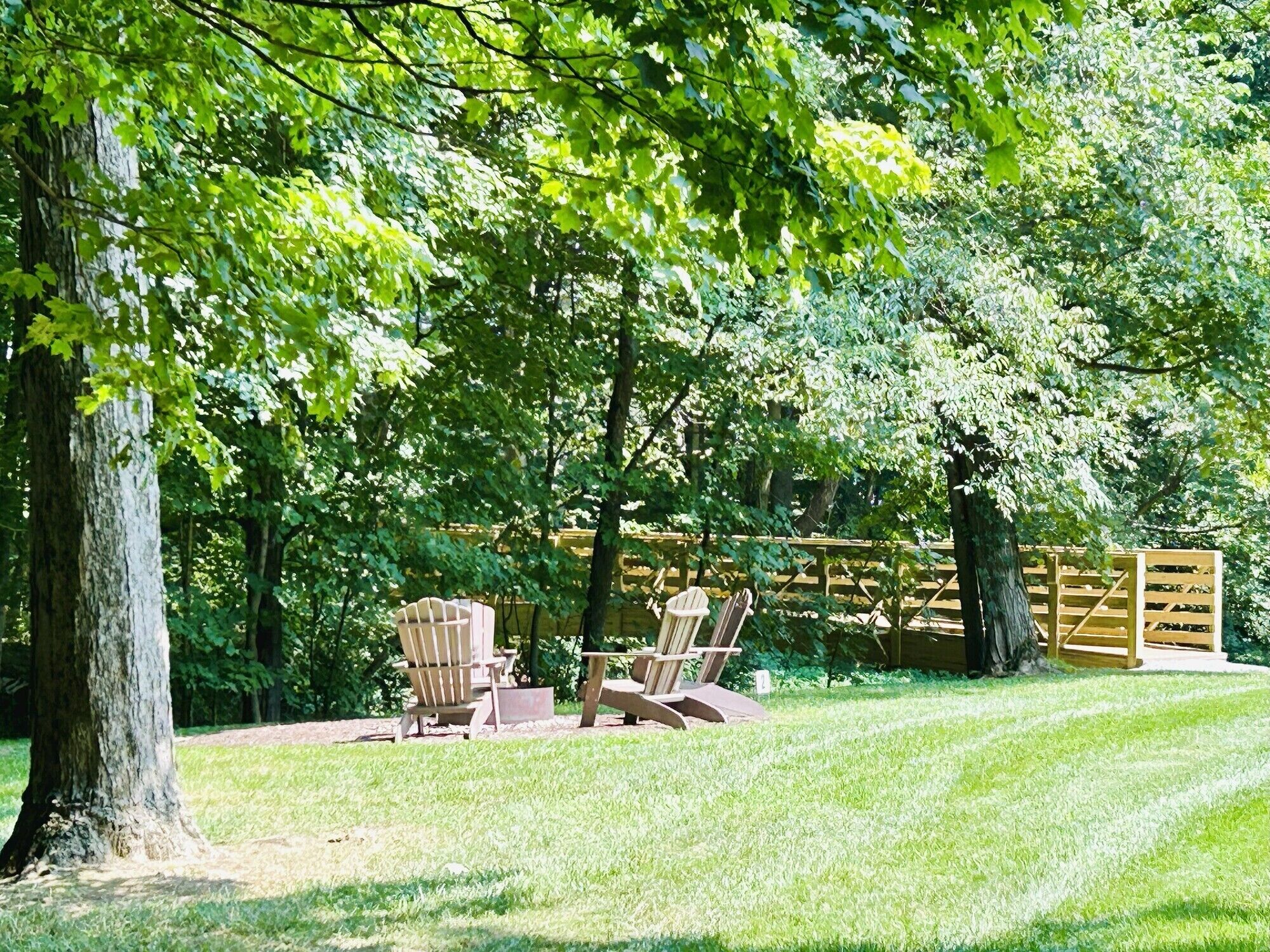 A backyard with a wooden deck, two Adirondack chairs, and a small table.