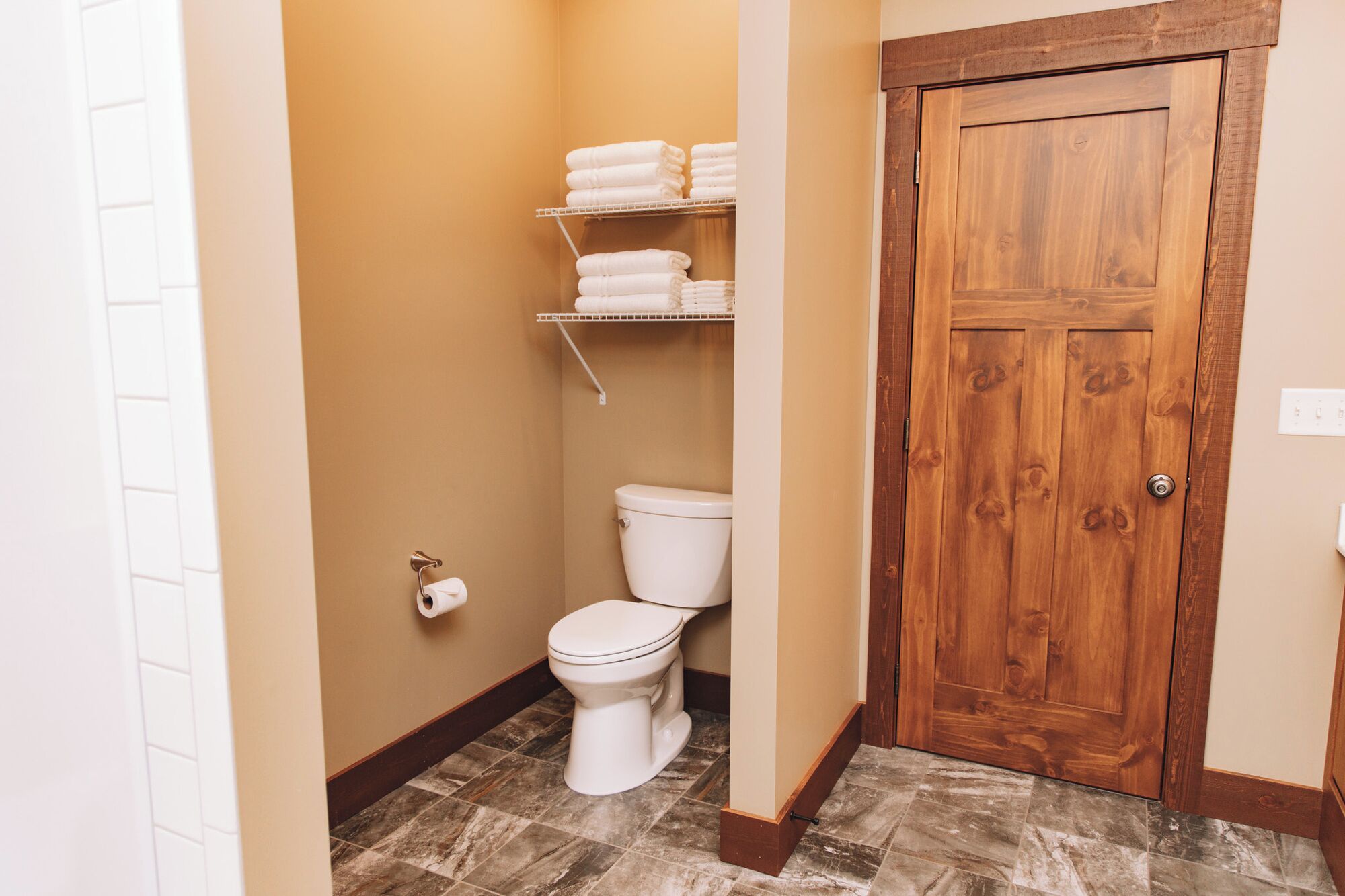 A bathroom with a toilet, a shelf with folded towels, and a wooden door.