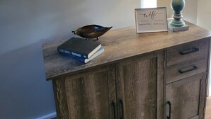 Un mueble de madera con un cartel enmarcados, una lámpara y un libro encima.