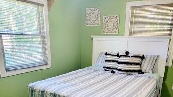 A bedroom with a bed, green walls, and a window with blinds.