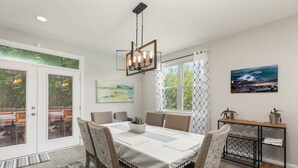 A dining area with a table set for six, surrounded by chairs, a hanging light fixture, and a view of the outdoors through glass doors. - New Modern Home in the heart of Downtown Durham (Durham)