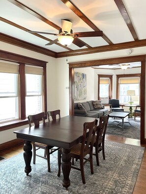 A dining area with a wooden table and chairs, a ceiling fan, and large windows. - Clean and Comfy Updated Apt in Convenient Location (Forest Park)