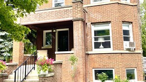 Un edificio in mattoni di due piani con un portico, una scalinata e un piccolo giardino.