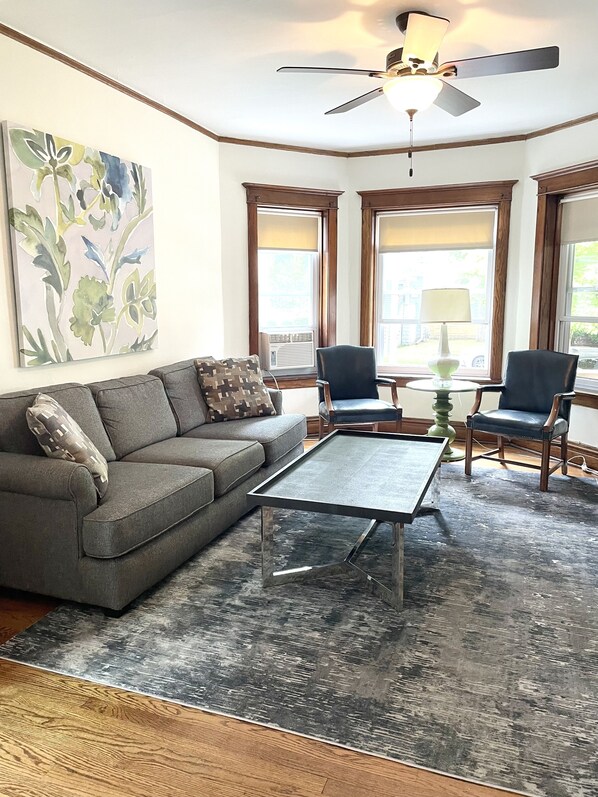 A living room with a gray sofa, two armchairs, a coffee table, and a ceiling fan. - Clean and Comfy Updated Apt in Convenient Location (Forest Park)
