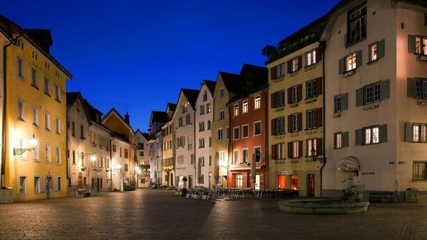 En historisk gade med traditionel europæisk arkitektur, brosten og udendørs siddepladser.