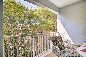 Enjoy the serene view of lush greenery from this balcony with a seating area and comfortable chair.