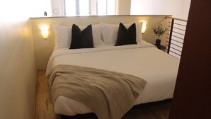 Una cama bien tendida con una manta color crema, almohadas blancas y un cabecero de madera.