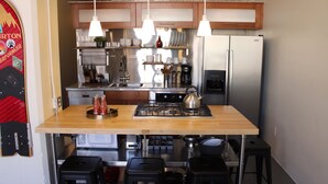 Cocina compacta con una isla central, electrodomésticos de acero inoxidable y lámparas colgantes.