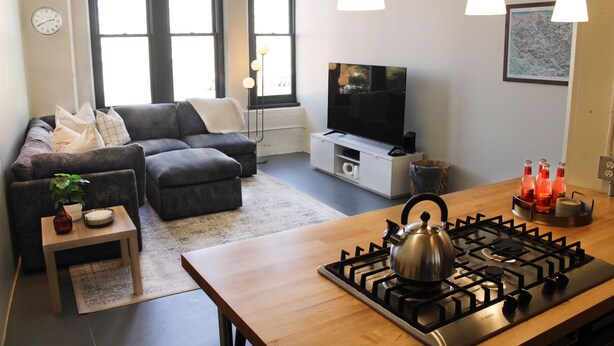 Una sala de estar moderna con un sofá, un televisor, una cocina con estufa a gas y una mesa de comedor.