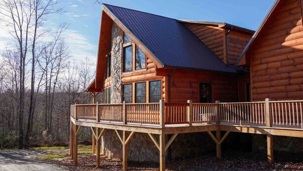 Una cabaña de troncos con base de piedra, una terraza de madera y techo de metal.