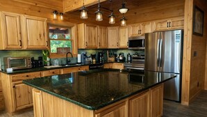 Cocina con armarios de madera, una isla grande, electrodomésticos de acero inoxidable e iluminación colgante.