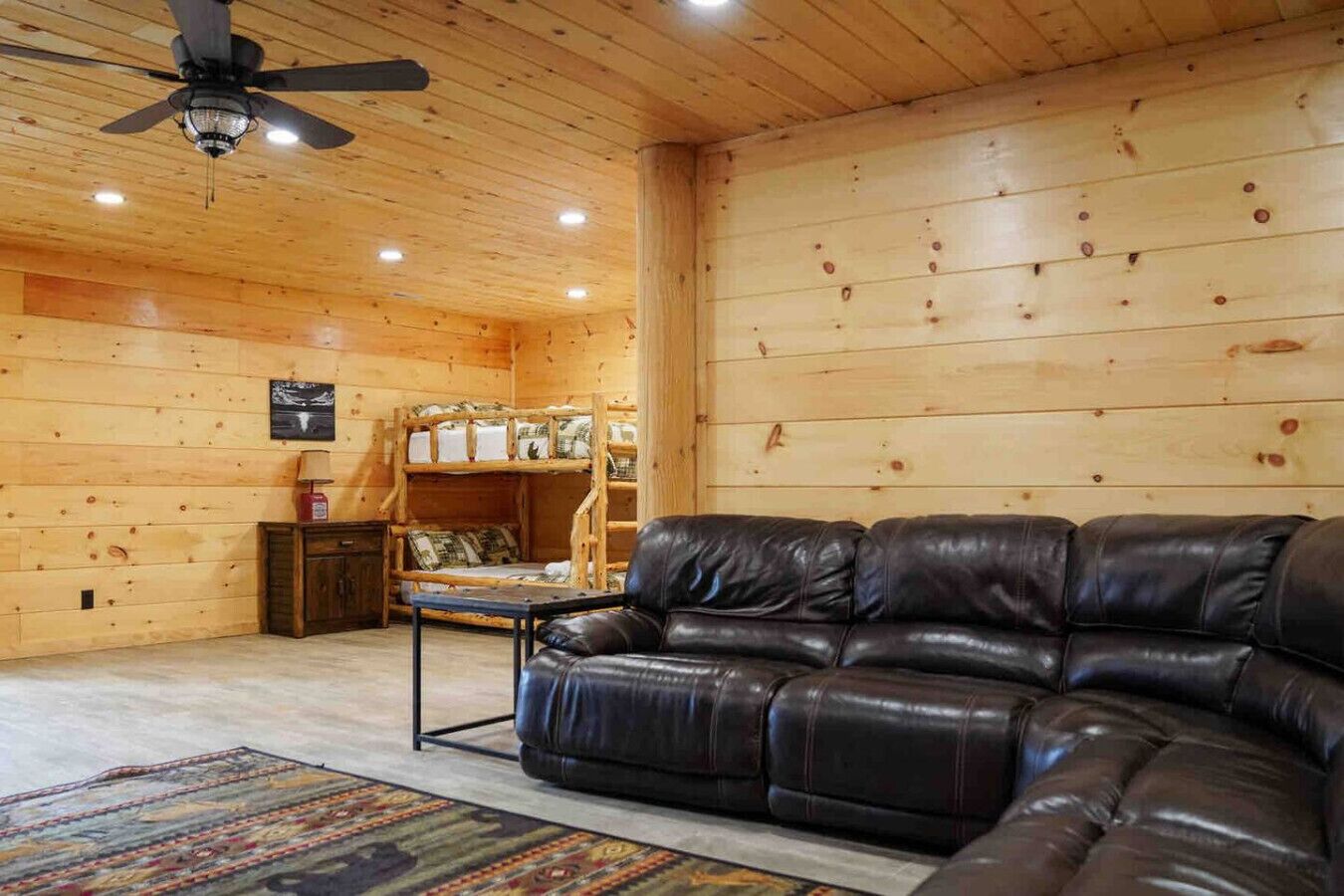 A log cabin interior with a leather sofa, a bunk bed, and a ceiling fan.