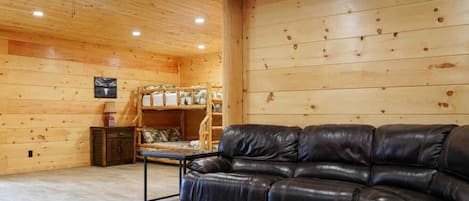 A log cabin interior with a leather sofa, a bunk bed, and a ceiling fan.