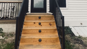 A two-story house with a wooden staircase leading to a black door with a 'WELCOME' sign.