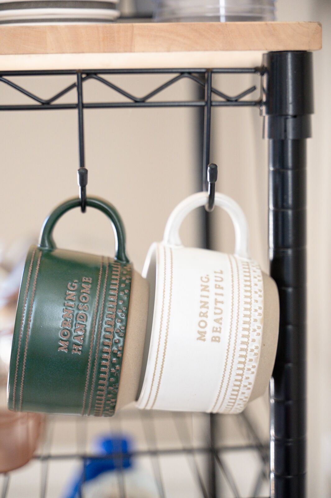 Two mugs hanging on a rack, one green and one white, both with text on them.