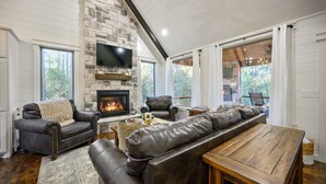 Una sala de estar acogedora con chimenea de piedra, mobiliario de cuero y amplias ventanas con vistas al exterior.