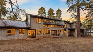 Una casa moderna de dos pisos con fachada de piedra, ventanas amplias y un área de patio cubierta.