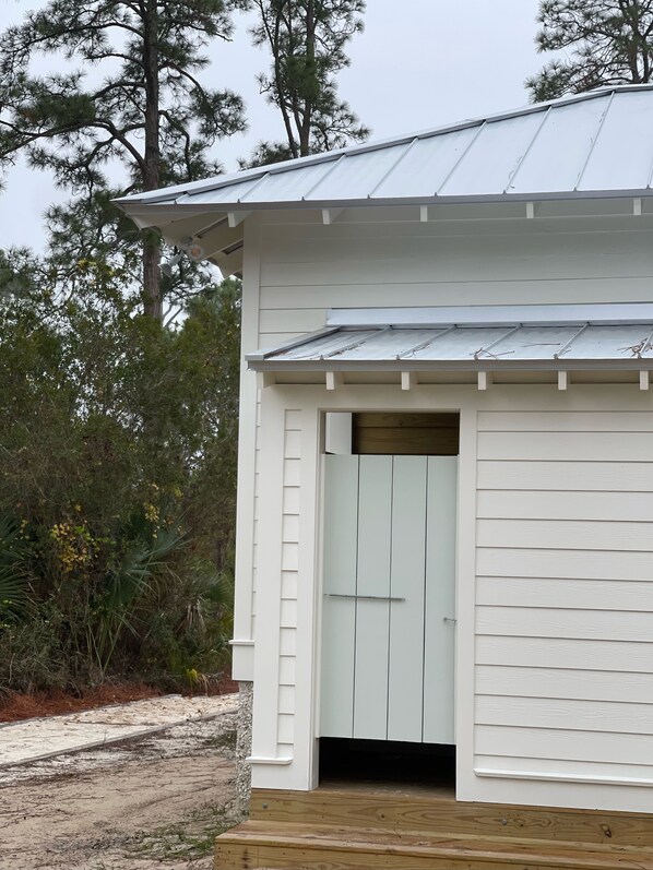 A white building with a metal roof, a wooden door, and a small porch.
