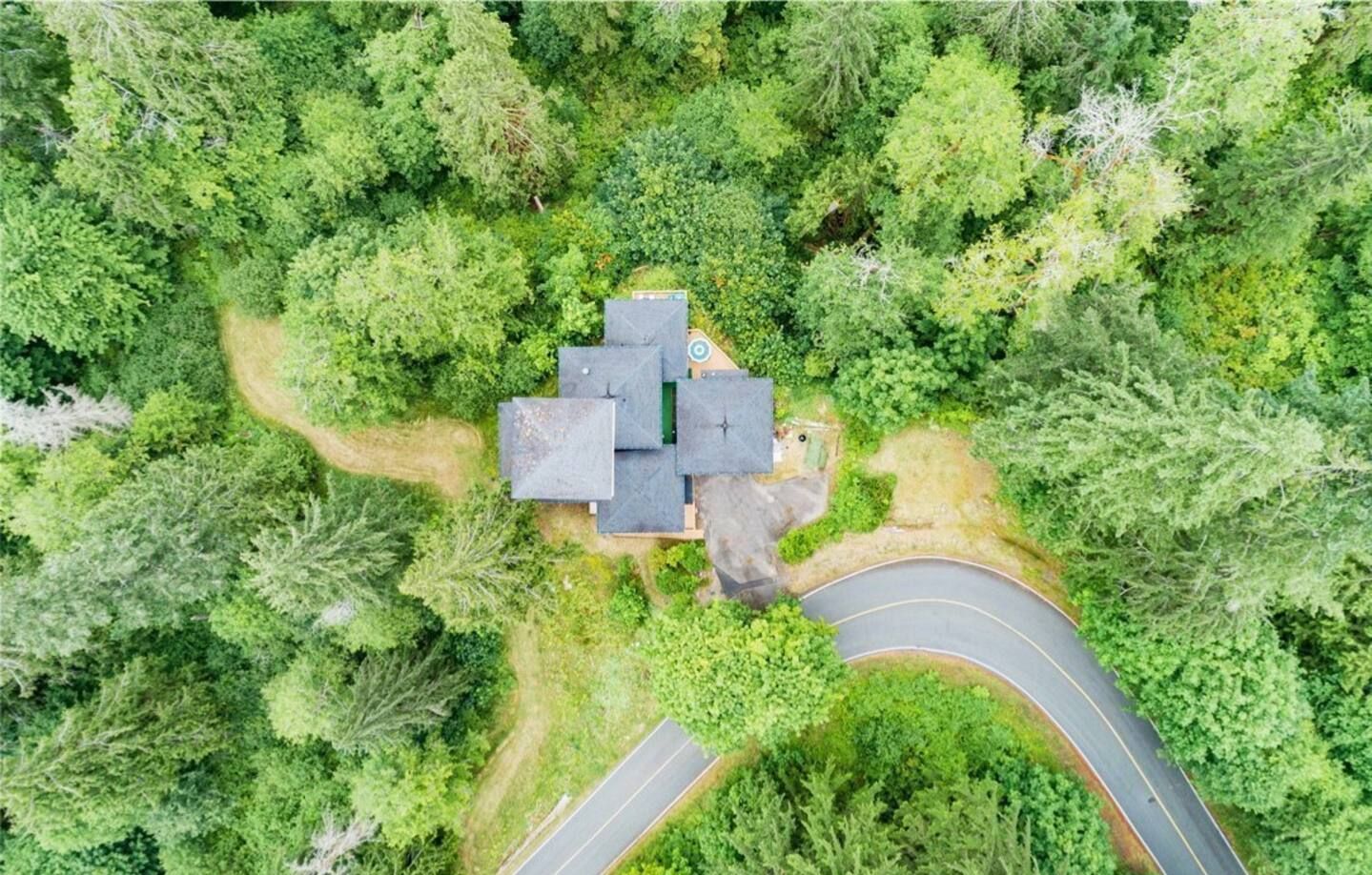 An aerial view of a house surrounded by dense forest, with a curved driveway leading to the entrance.