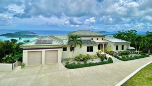 Una casa de dos pisos con garaje, paneles solares y vista al océano.
